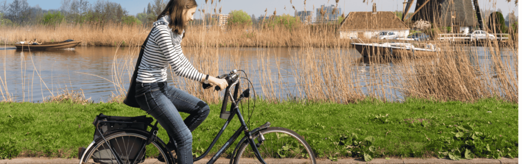 Vrouw fietst langs een meer met molen op de achtergrond, symboliseert fietsverzekeringen vergelijken voor de beste keuze.