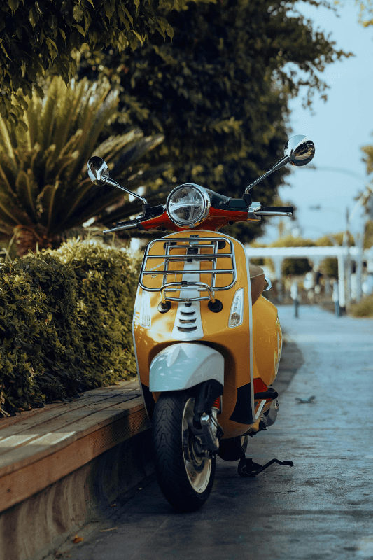 Geparkeerde gele scooter langs een groene omgeving. Vind de goedkoopste scooterverzekering met een lage premie.