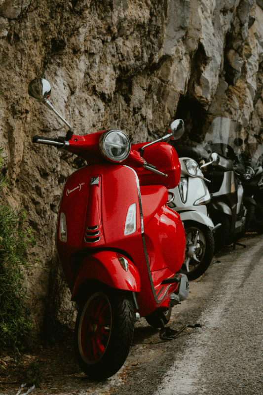 Rode scooter geparkeerd langs een rotswand. Vergelijk de goedkoopste scooterverzekeringen en bespaar op je premie.