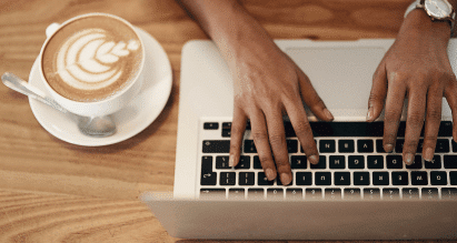 Zzp'er werkt op laptop in koffiezaak met cappuccino op tafel