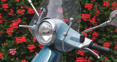 Blauwe scooter met windscherm voor een haag met rode bloemen