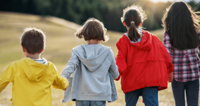 Vier kinderen lopen hand in hand buiten in een open veld tijdens een schoolreisje.
